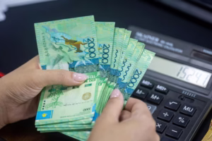Person counting Kazakhstani Tenge banknotes next to a calculator. Financial concept.
