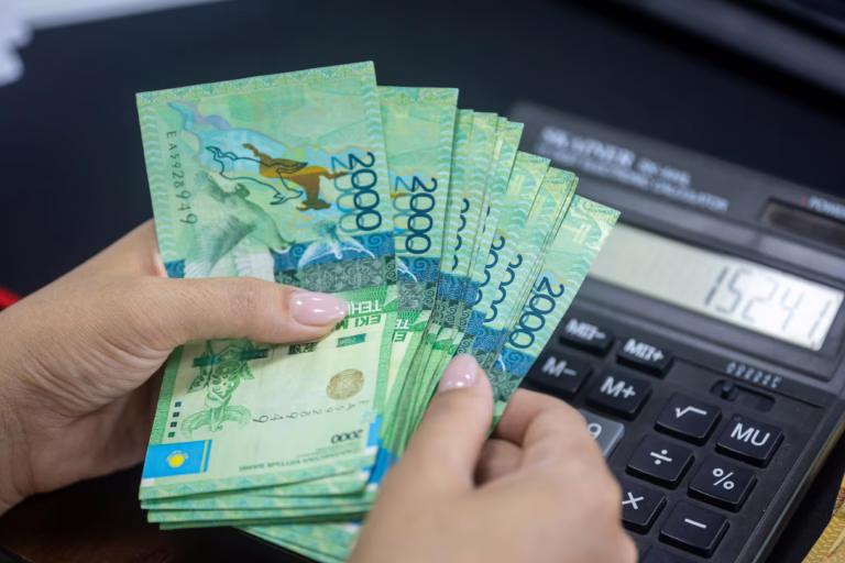 Person counting Kazakhstani Tenge banknotes next to a calculator. Financial concept.