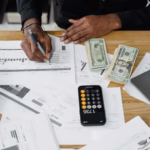 Man working on accounting and financial reports with calculator, money, and laptop on a desk.