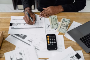 Man working on accounting and financial reports with calculator, money, and laptop on a desk.